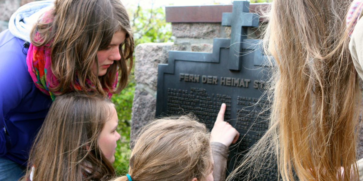 Jugendliche lesen die Namen auf einer Gedenktafel